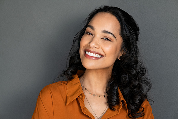 Smiling woman with short hair, wearing a brown top and standing against a dark background.
